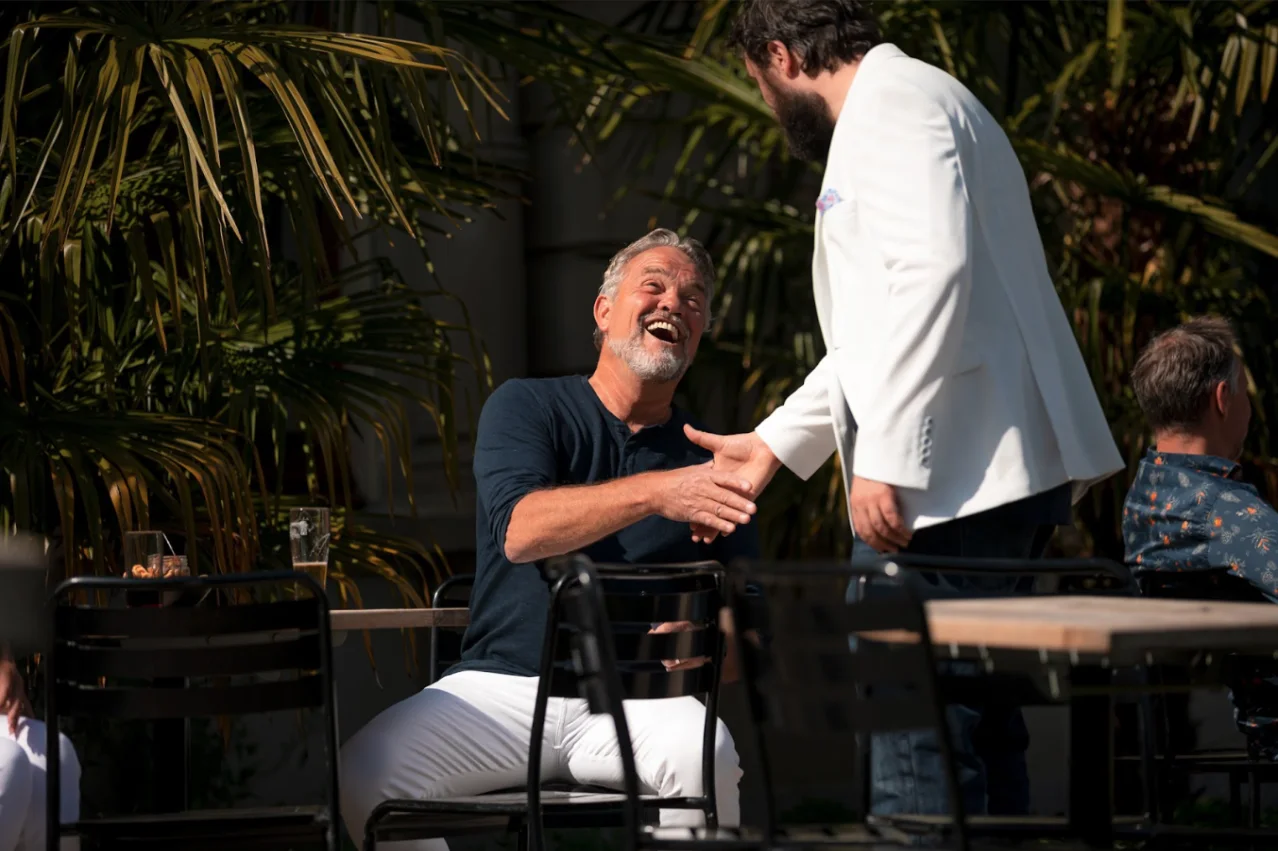 Twee ondernemers schudden elkaar lachend de hand op een zonnig terras