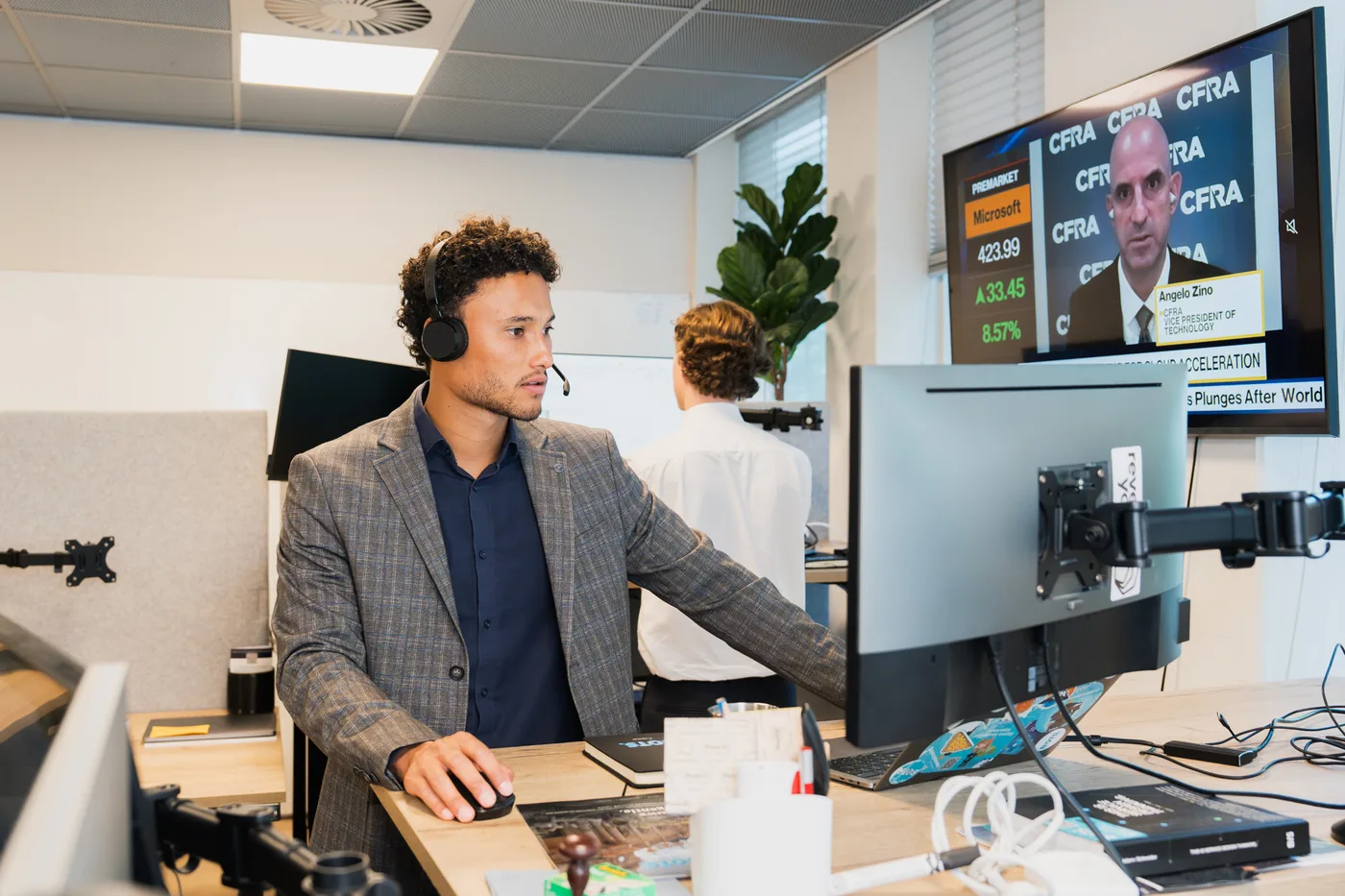 Een specialist van BOTS Capital met headset aan de handelsdesk, met een beursscherm op de achtergrond